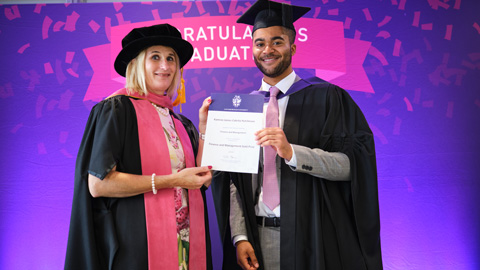 Two people in graduation attire; one hands a certificate to the other